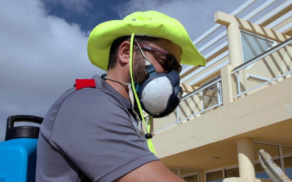 técnico de Anviana vestido con su uniforme, sombrero y gafas para protegerlo del sol y mascara profesional para evitar que respire los productos.